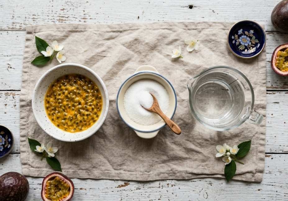 Flat lay view of passion fruit syrup ingredients including passion fruit pulp, white sugar, and water on a linen napkin.